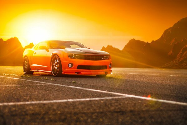Camaro MOP orange sur fond de montagnes et le soleil