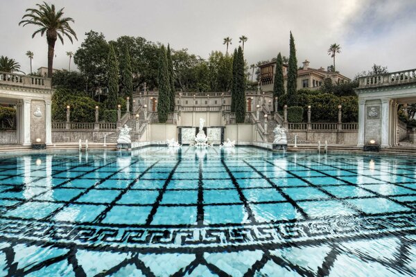 Piscine bleue près du parc de villégiature avec des escaliers et des cyprès