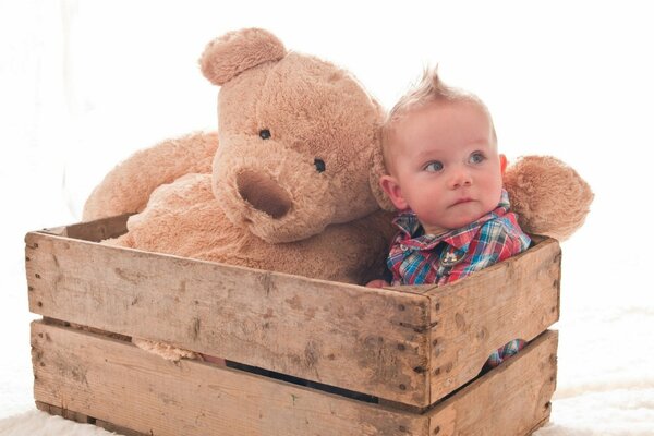 Garçon avec un ours en peluche dans une boîte en bois