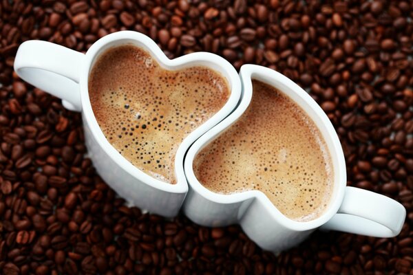 Deux tasses de café avec forme de coeur sur fond de grains de café