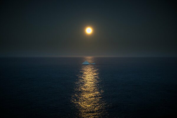 Au milieu de la mer à la lumière de la pleine lune flotte un iceberg
