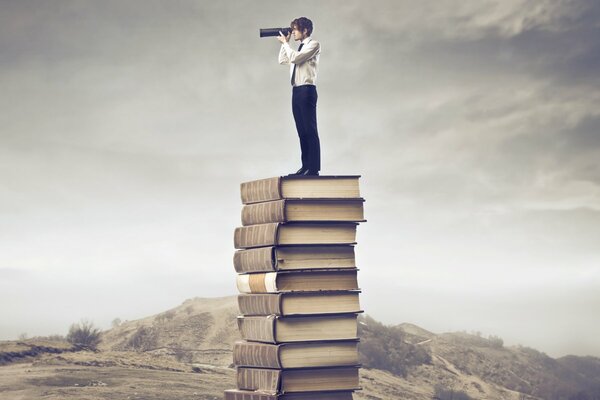 Le gars regarde dans la lorgnette debout sur une pile de livres