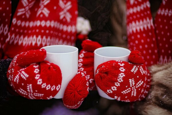 Les mains dans des gants rouges tiennent un verre avec du thé