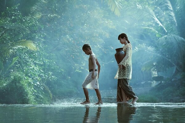 Fille avec une cruche et un garçon marchent sur la rivière dans la jungle