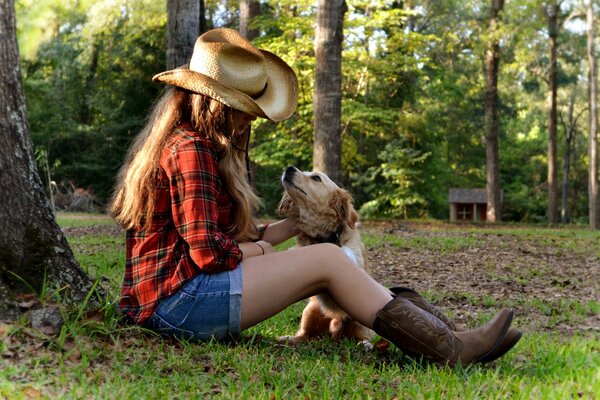 Fille au chapeau caresse un chien sous un arbre