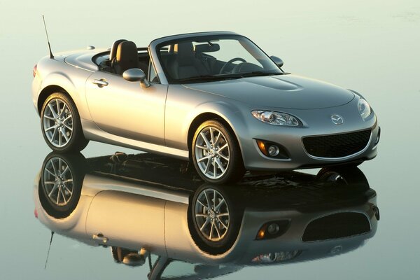 Une Mazda grise sur une décapotable se dresse sur une surface en miroir