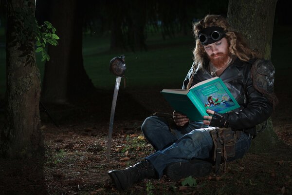 Un homme aux cheveux longs avec une barbe lit un livre de contes de fées dans la forêt