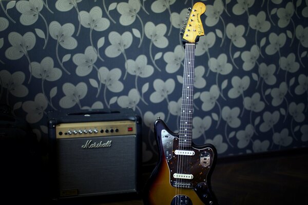 Une guitare avec un amplificateur se tient contre le mur
